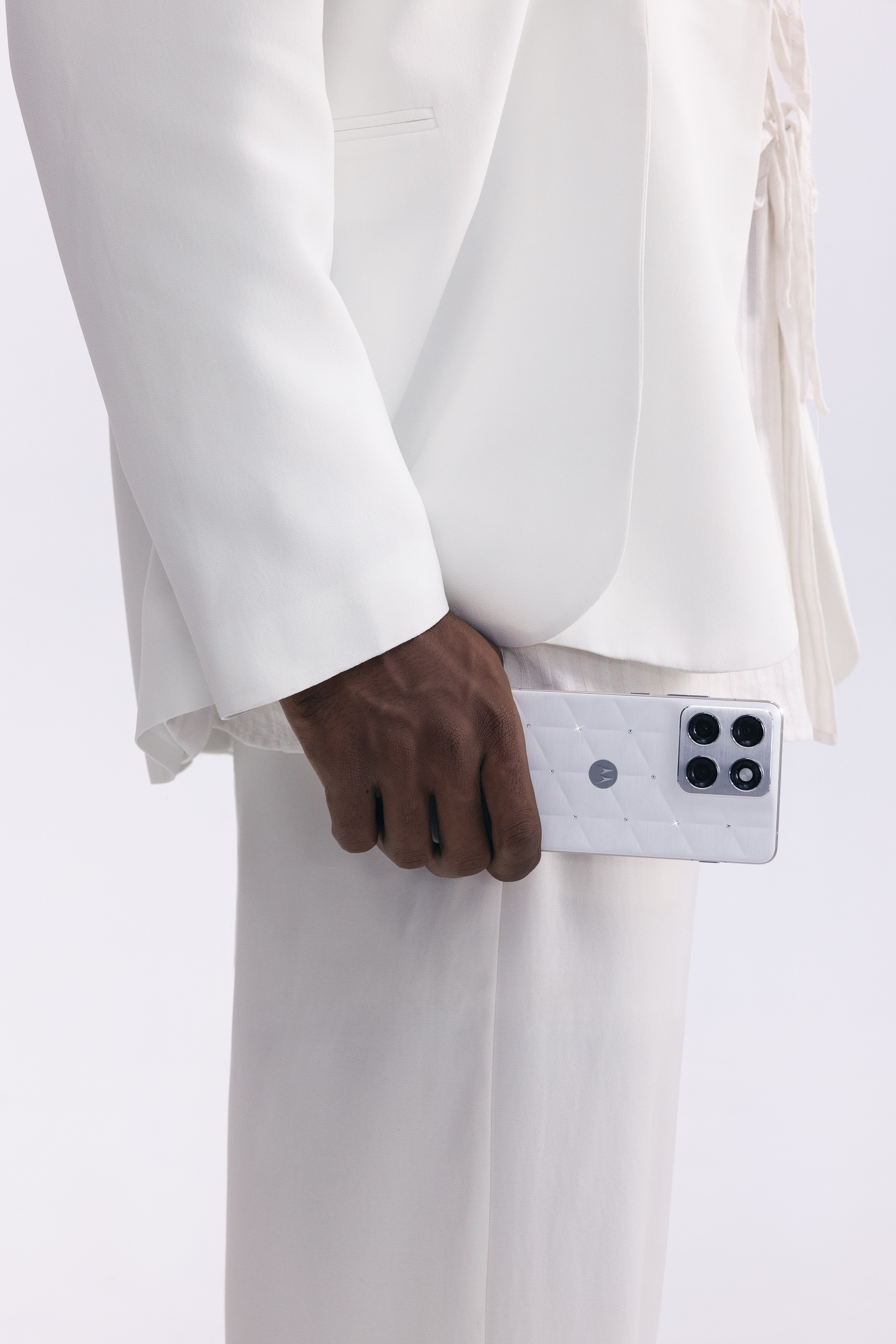 Detail of a hand in a white suit holding a white quilted phone at hip height