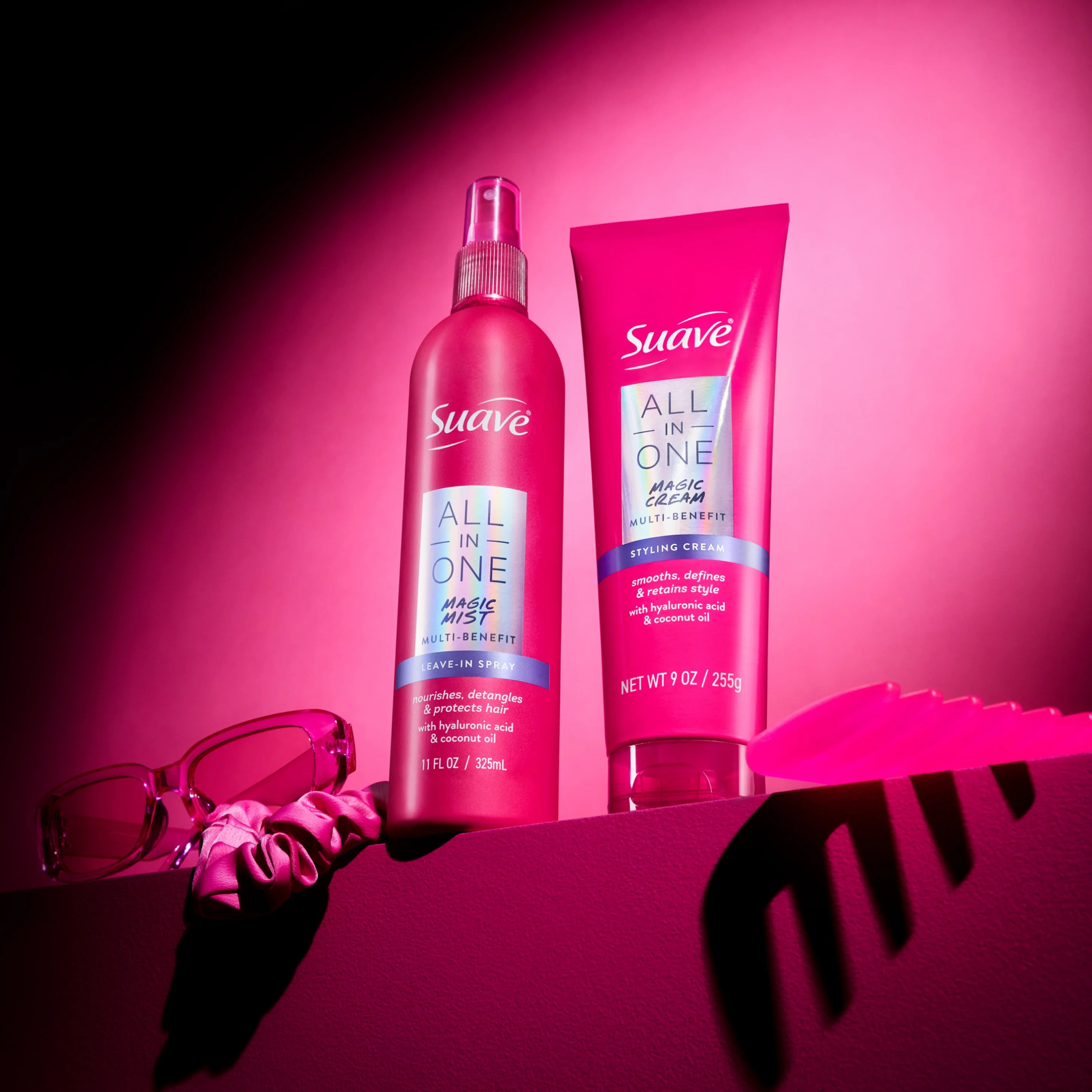 Product shot of Suave All In One Magic Mist spray and Magic Cream tube on a pink ledge with pink sunglasses, scrunchie and comb