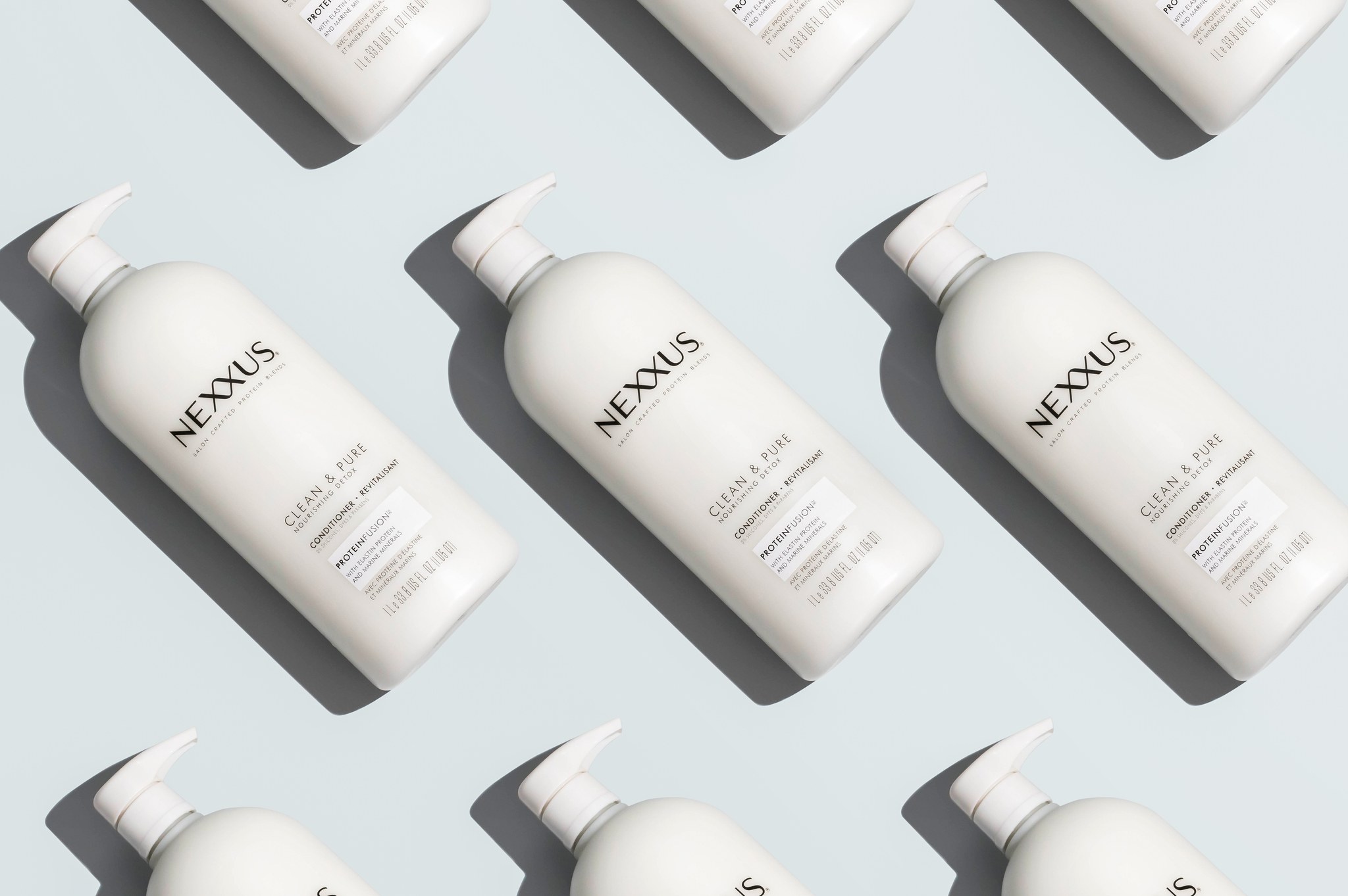 Repeating diagonal pattern of white Nexxus Clean & Pure conditioner pump bottles casting shadows on a pale blue surface