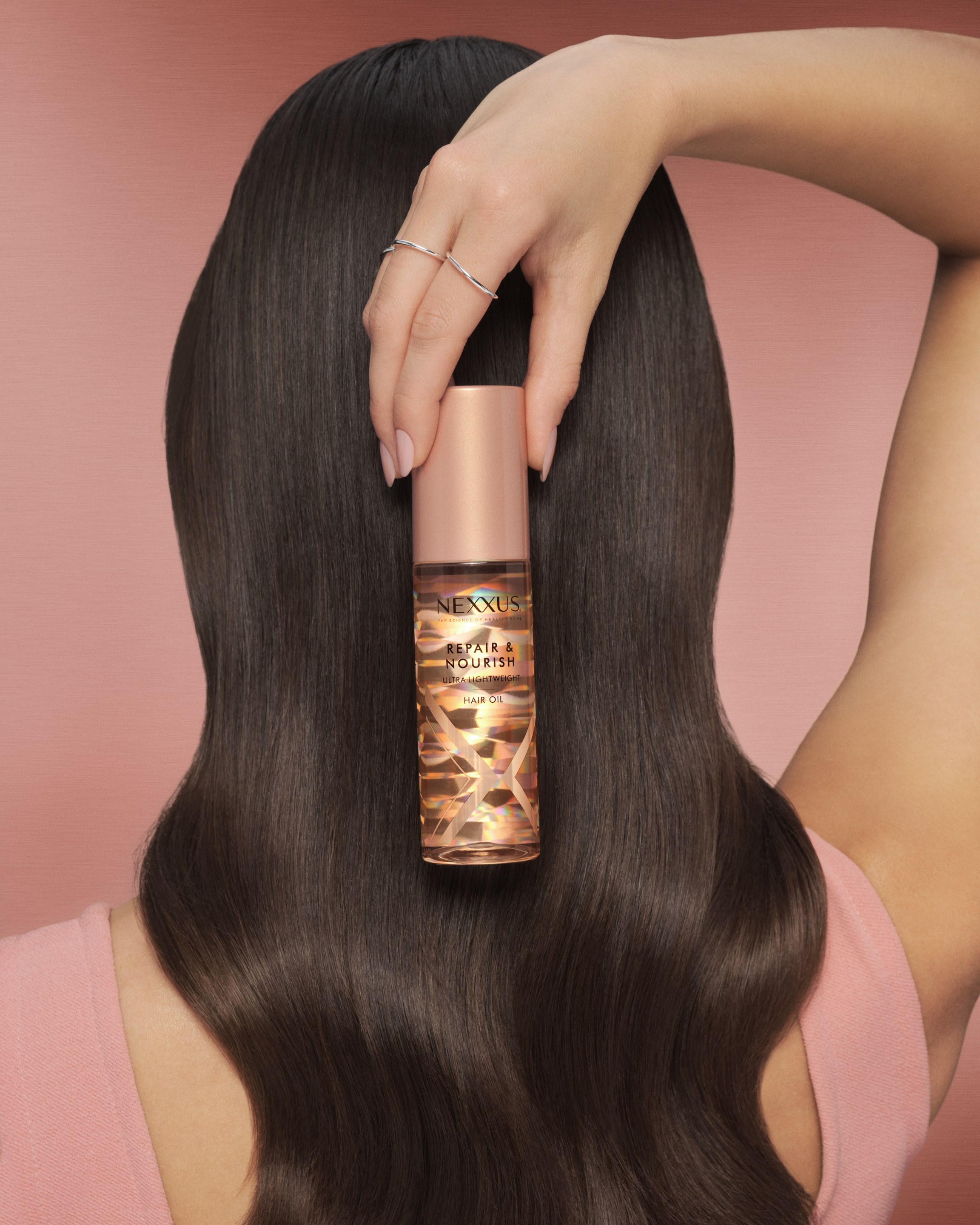 Woman seen from behind with long glossy dark hair holds a Nexxus bottle at the back of her head