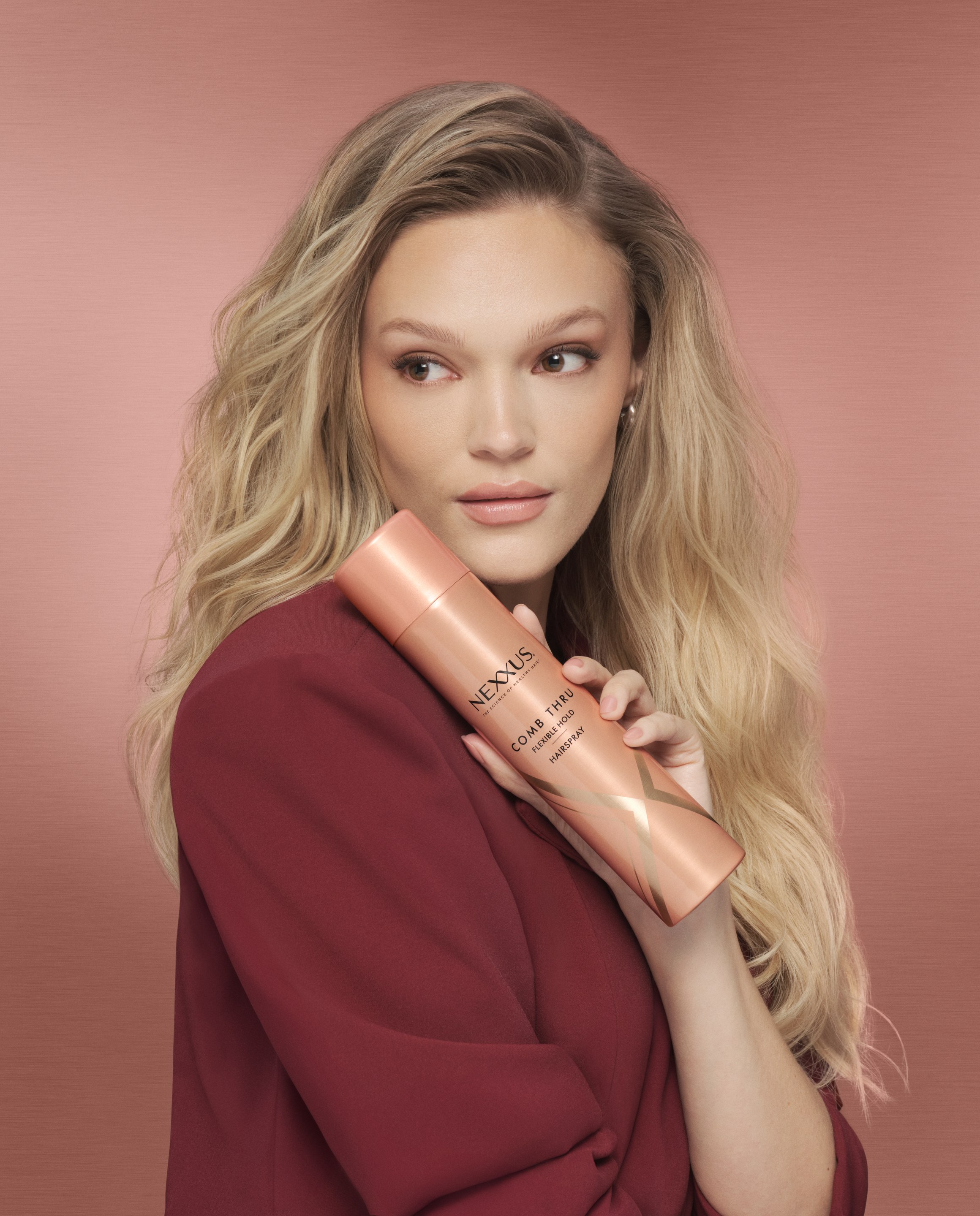 Blonde model in a burgundy blazer holds a pink Nexxus bottle beside her long waves