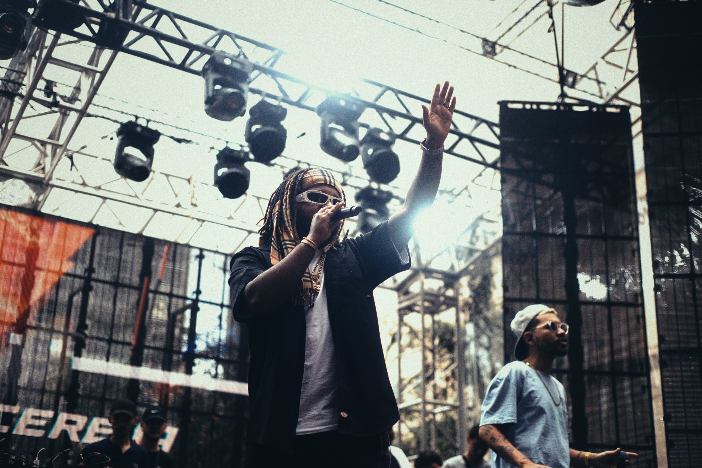 An artist on stage with a raised hand, lights rigged above