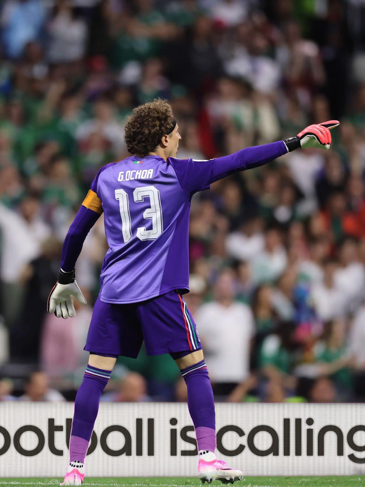 Goalkeeper in a purple G. Ochoa 13 kit points across the field, crowd behind and a "football is calling" board