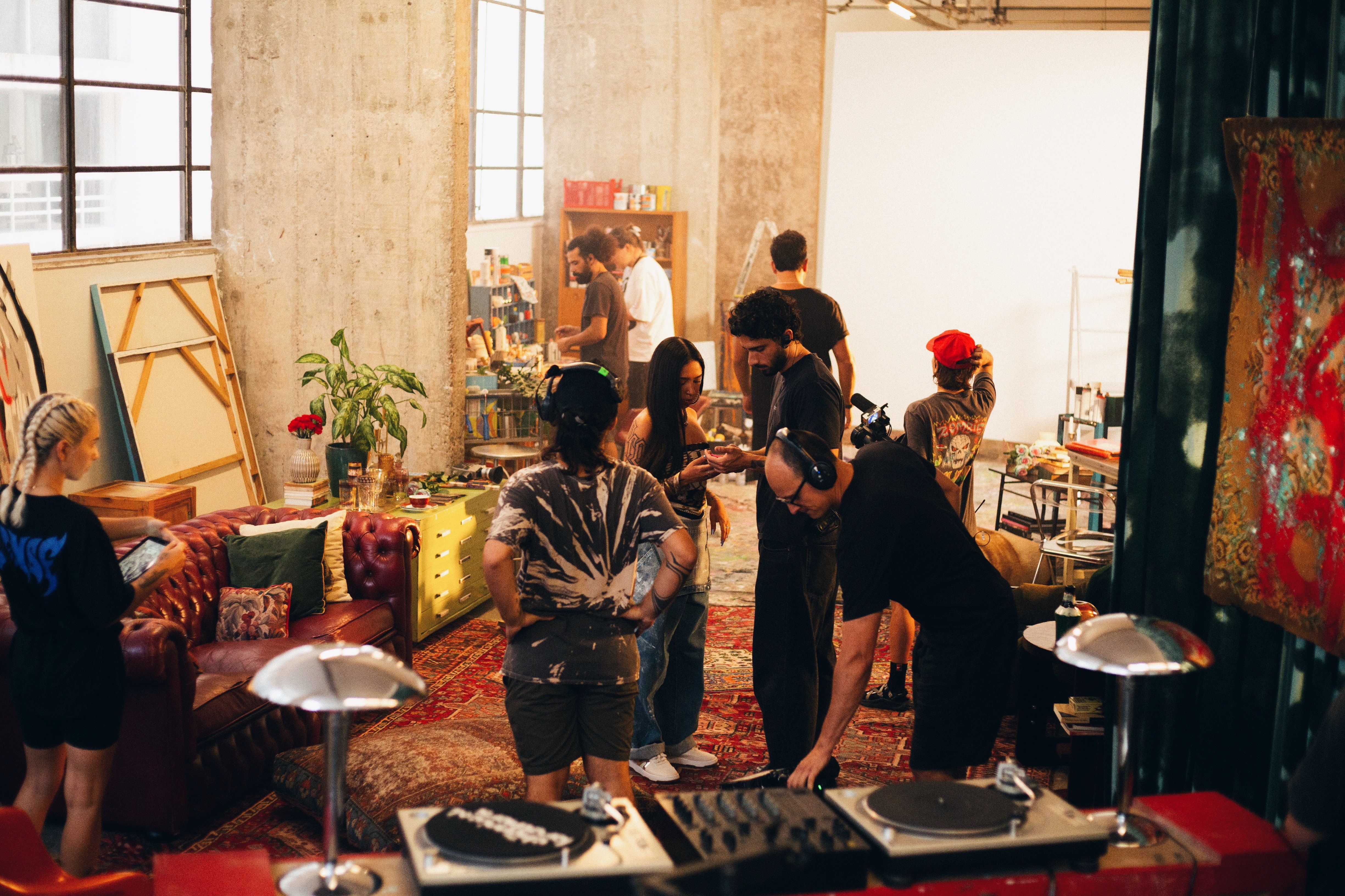 Behind the scenes in a loft set with turntables, rugs and a leather sofa, crew in headphones and cameras
